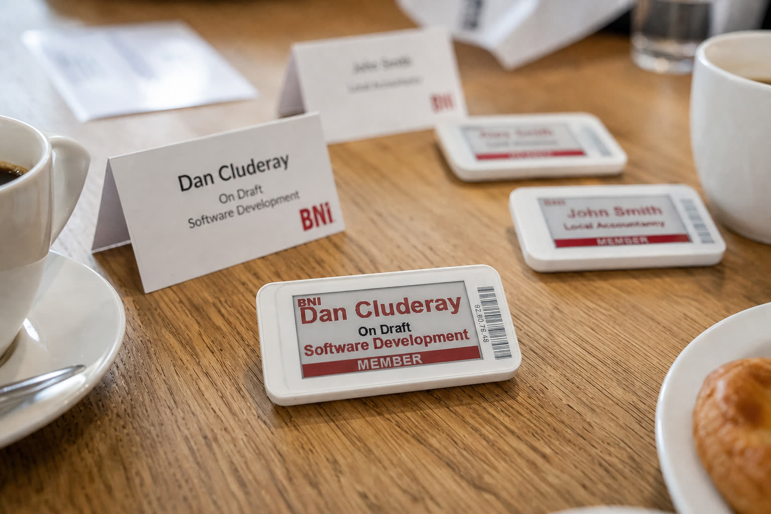 E-ink badges on a networking table next to coffee and a pastry